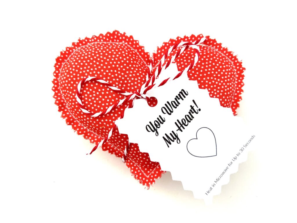 Two red heart-shaped items with white polka dots, tied together with a string, perfectly crafted as DIY hand warmers. A charming tag reads "You Warm My Heart!.