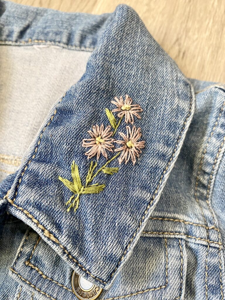 Close-up of denim jacket collar with embroidered pink flowers and green leaves.