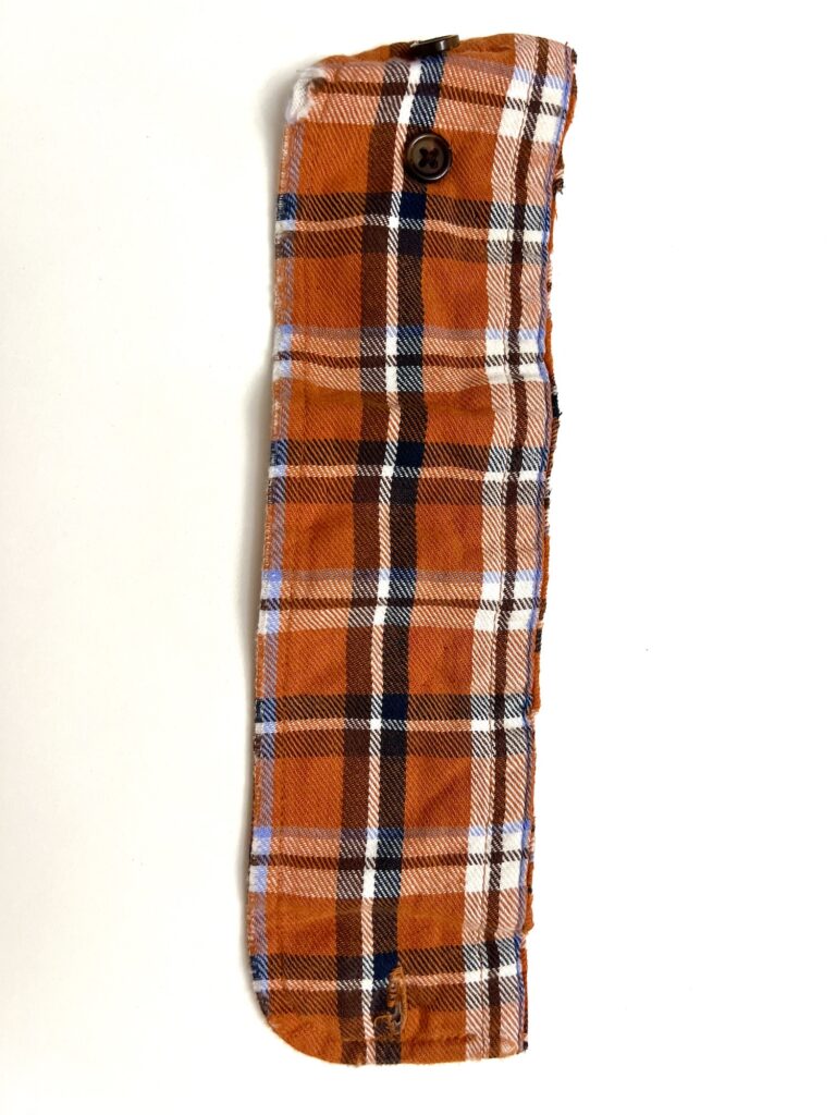 Orange and white plaid fabric item with a button on one end, displayed against a white background.