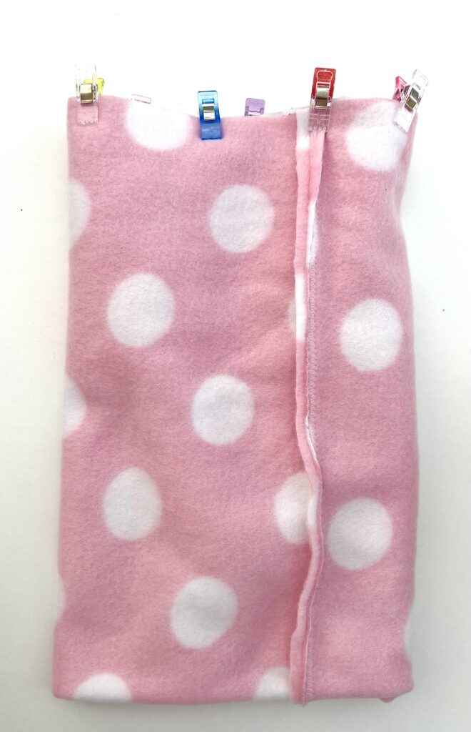 A pink fabric with white polka dots is folded and held with colorful clips on one side.