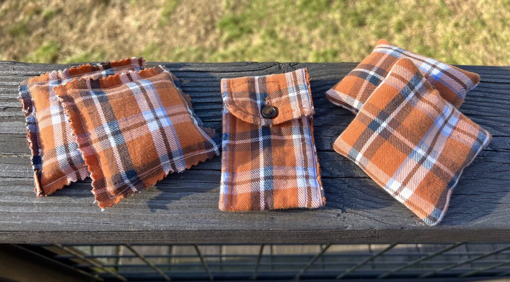 Plaid flannel hand warmers and a matching chapstick holder rest on a wooden surface.