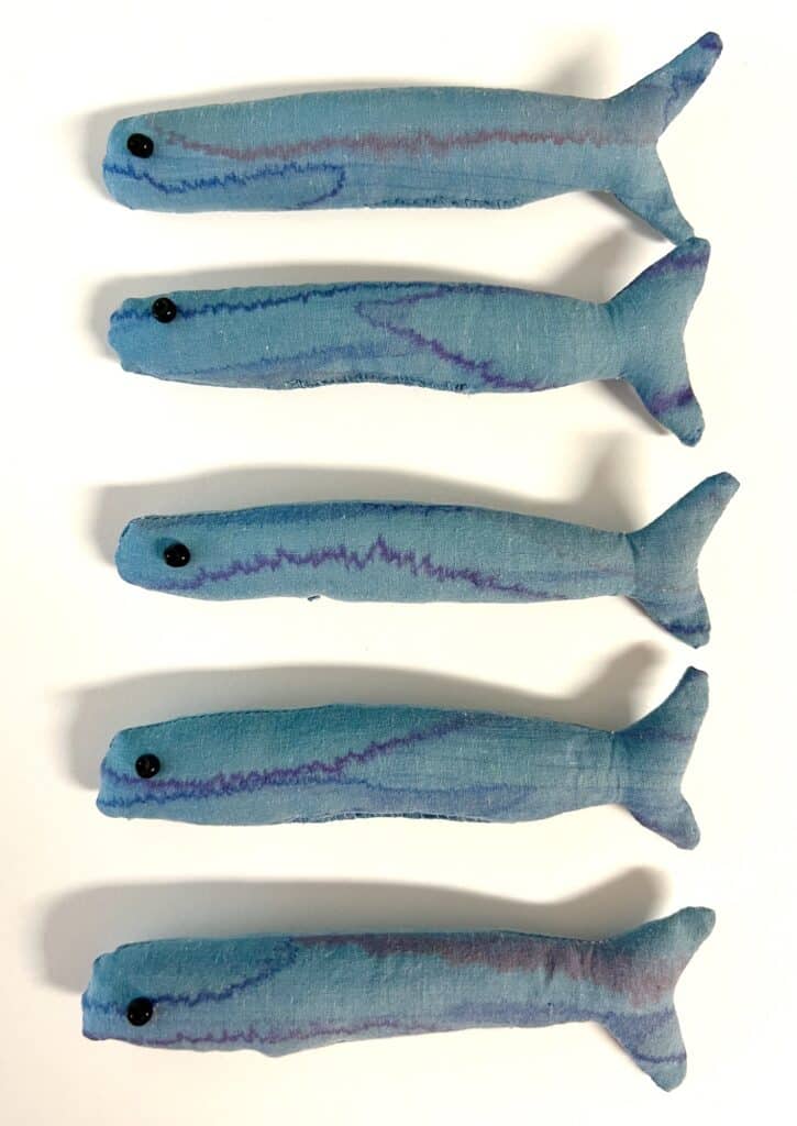 Five blue fabric sardines with black button eyes are arranged in a vertical line on a white background.