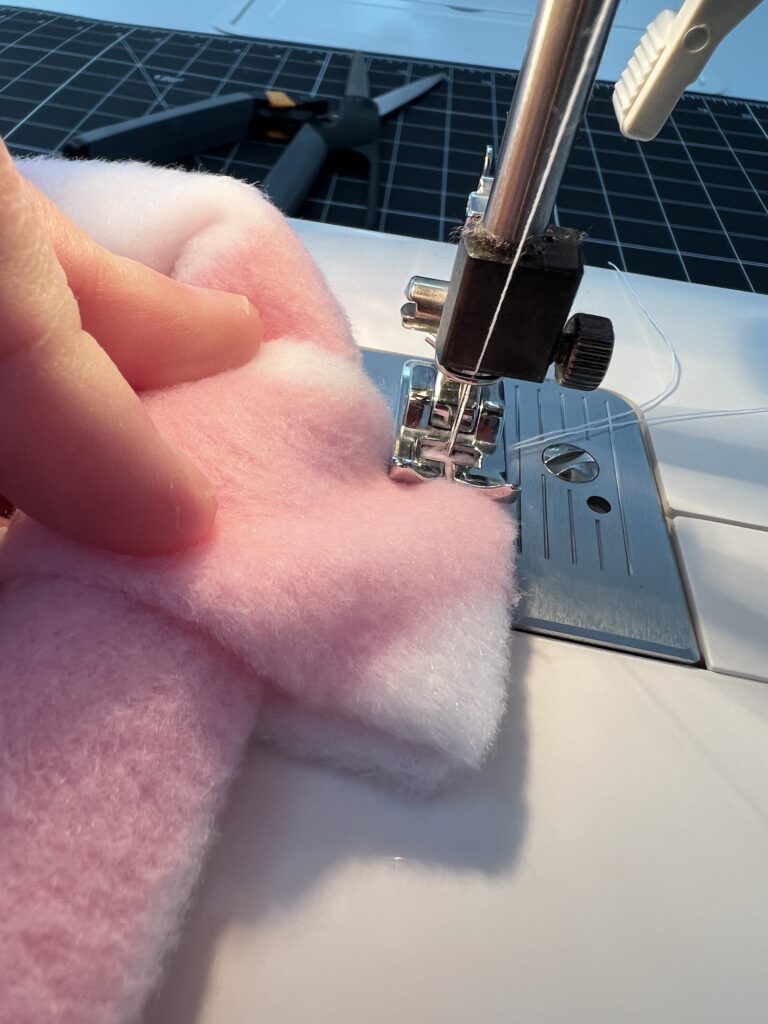 A hand skillfully guides pink and white fabric under a sewing machine needle, crafting a cozy fleece headband.