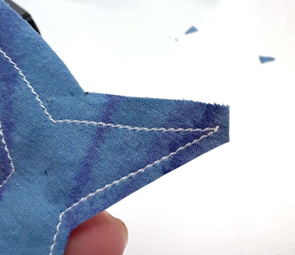 Close-up of a blue fabric star with visible white stitching along the edges, held by a hand against a white background, reminiscent of the ocean where sardines swim gracefully.