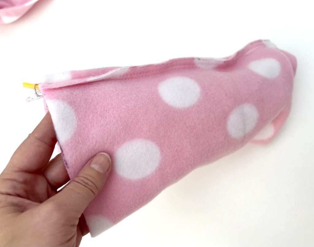 A hand is holding a pink fleece fabric with white polka dots, folded in half, with a yellow clip partially visible at one end.