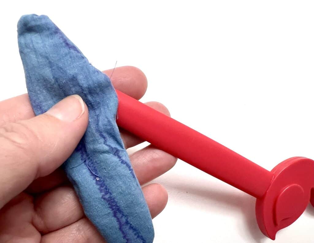 A hand holding a deflated blue balloon next to a red plastic balloon pump, reminiscent of packed sardines, rests against a white background.