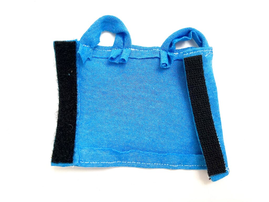 A small blue fabric pouch with two loops at the top and two black Velcro strips on the sides.