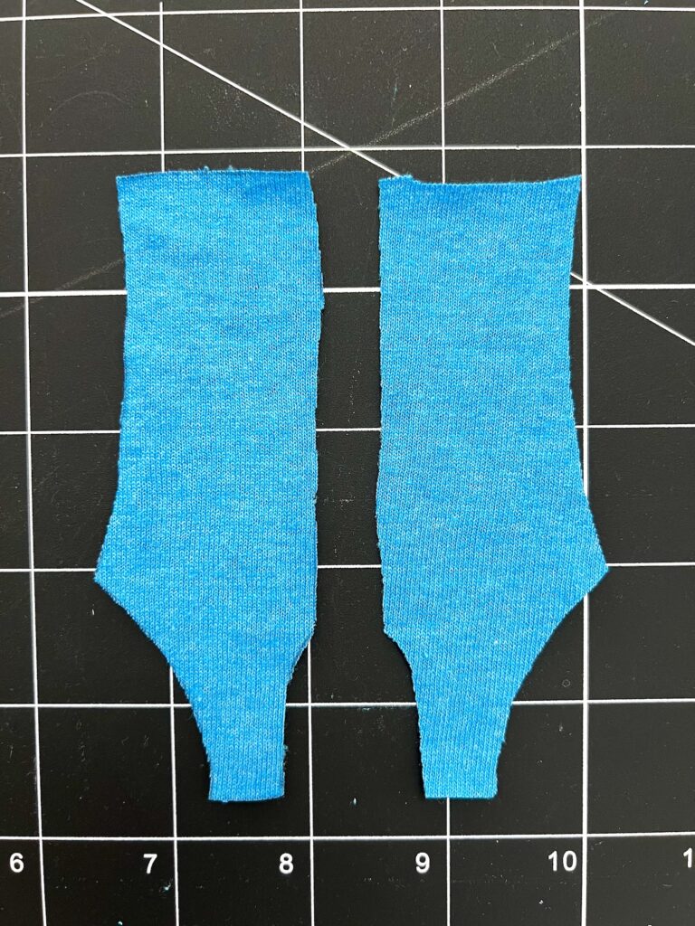 Two pieces of blue swimsuit fabric cut in a specific shape are placed on a black grid cutting mat.