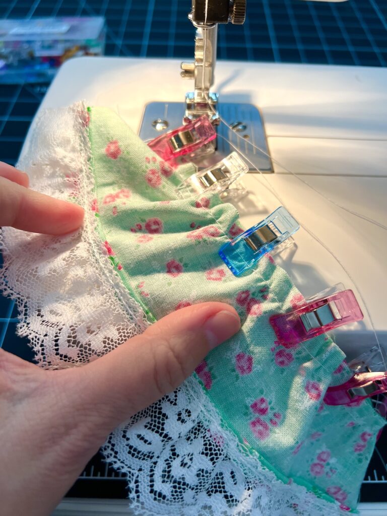 Sewing machine stitching lace to floral fabric, plastic clips securing it for the perfect tiered skirt. A hand carefully adjusts the material.