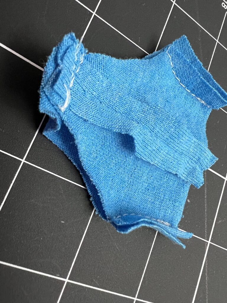 A small piece of blue fabric, resembling miniature shorts, placed on a black grid-patterned surface.