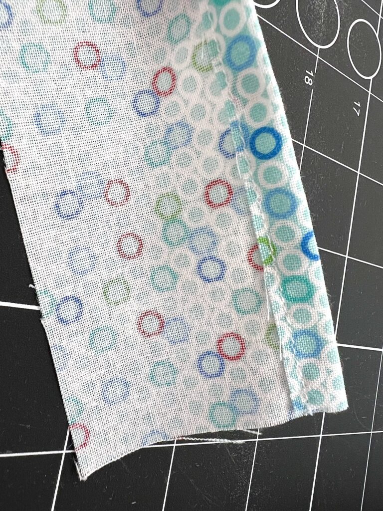 A piece of fabric with a pattern of overlapping circles in blue, green, and red on a black cutting mat with white grid lines.