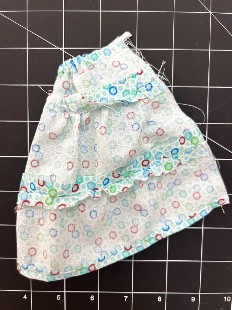 A small piece of fabric with a colorful circular pattern and a ruffled seam lies on a black cutting mat marked with a grid and measurement numbers.