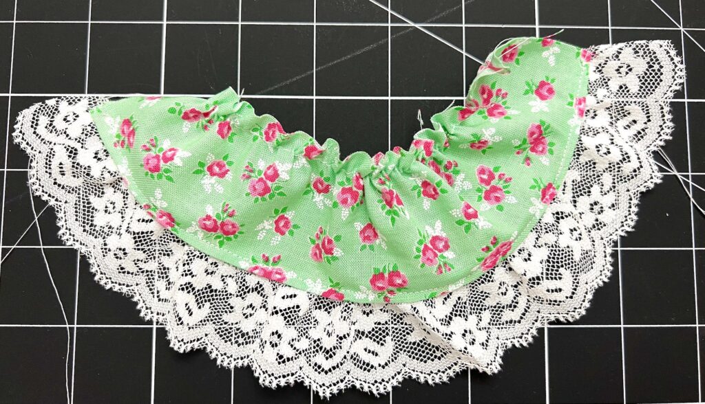 A tiered skirt features green fabric with a pink floral pattern and white lace trim, expertly gathered in the middle, all set against a striking black grid background.