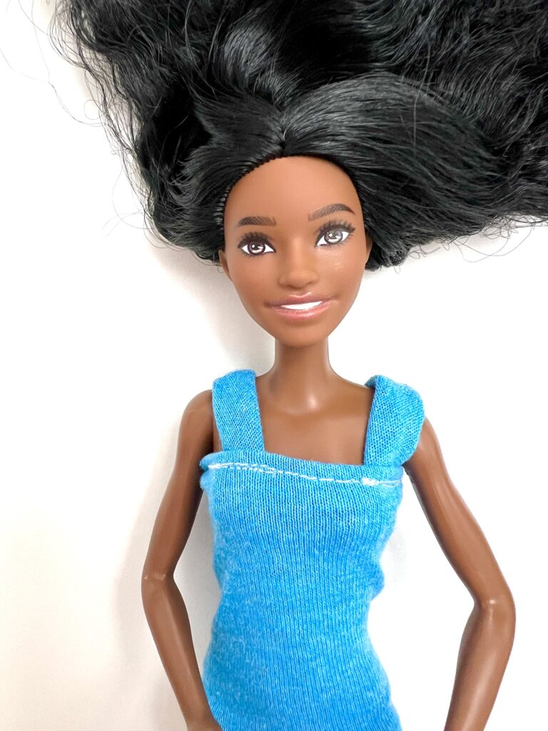 A doll with long black hair and a sleeveless blue dress lies on a white background.