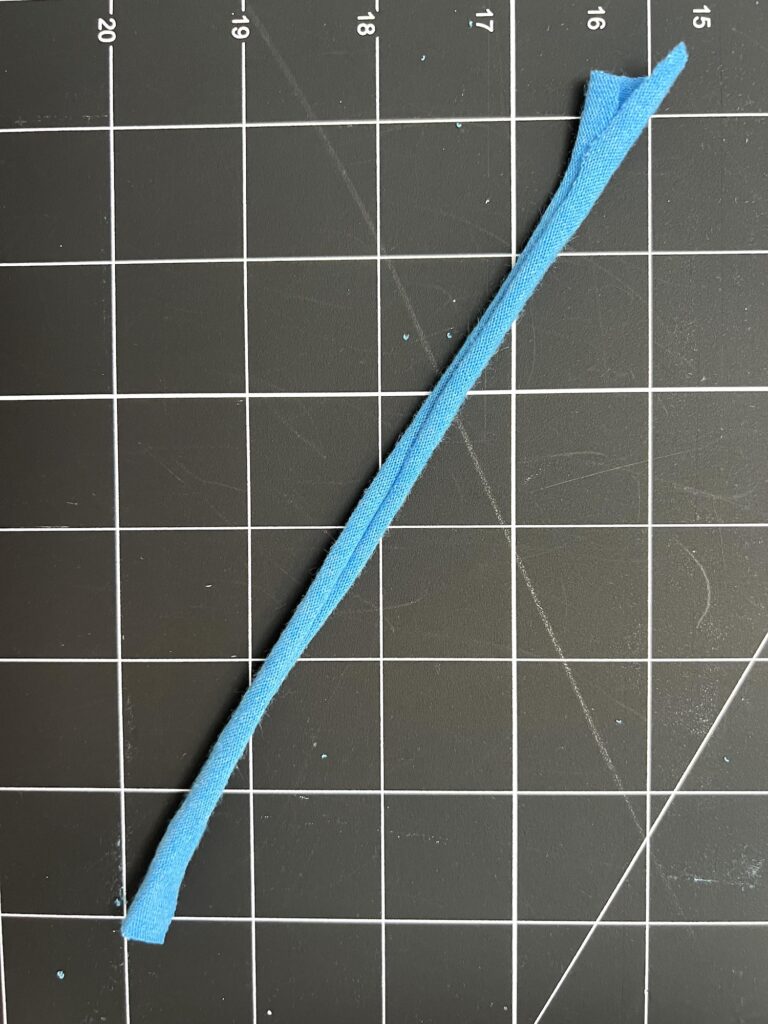 A blue fabric strip is placed diagonally on a black grid cutting mat with white measurement lines.