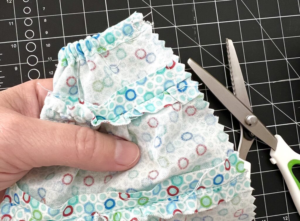 Hand holding fabric with a colorful circular pattern next to pinking shears on a cutting mat.