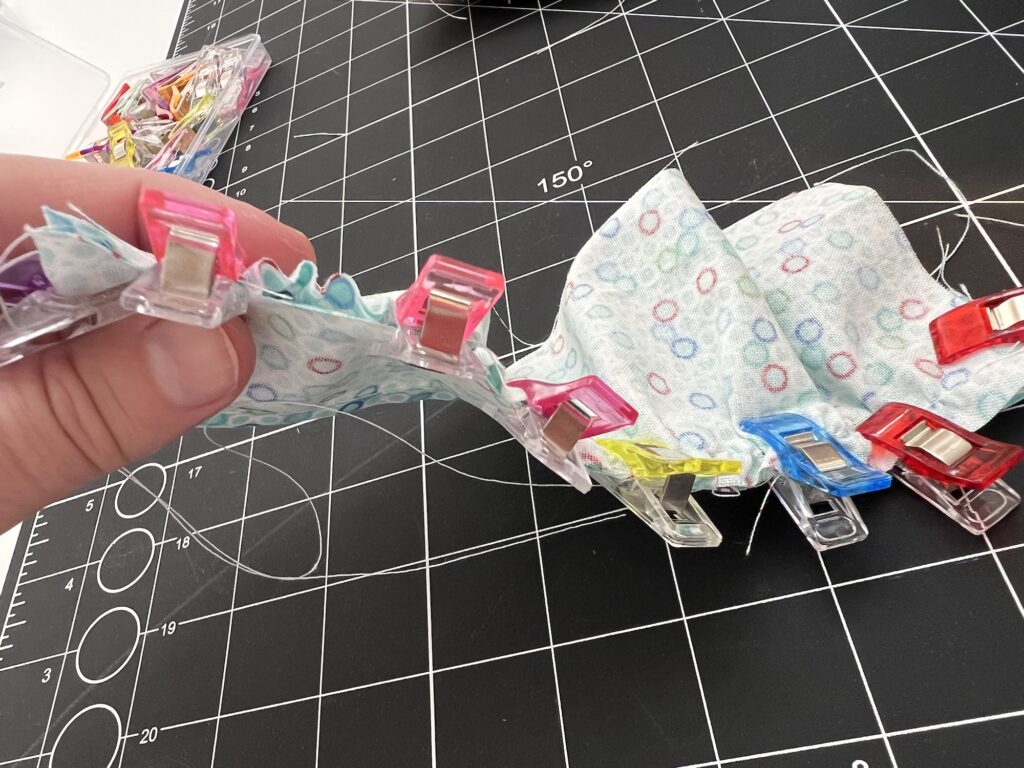 A hand holds fabric secured with colorful clips on a black grid cutting mat.