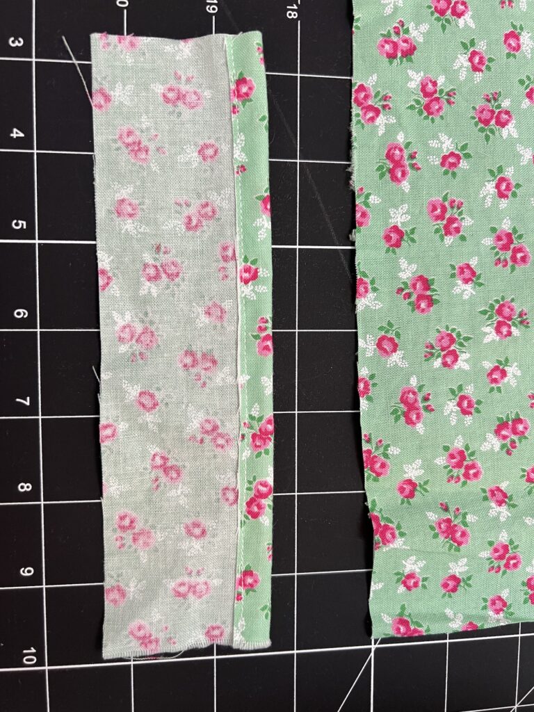 Two pieces of green fabric with pink floral patterns rest on a cutting mat. The left piece is narrow and folded; the right piece, wider and flat, seems perfect for crafting a tiered skirt.