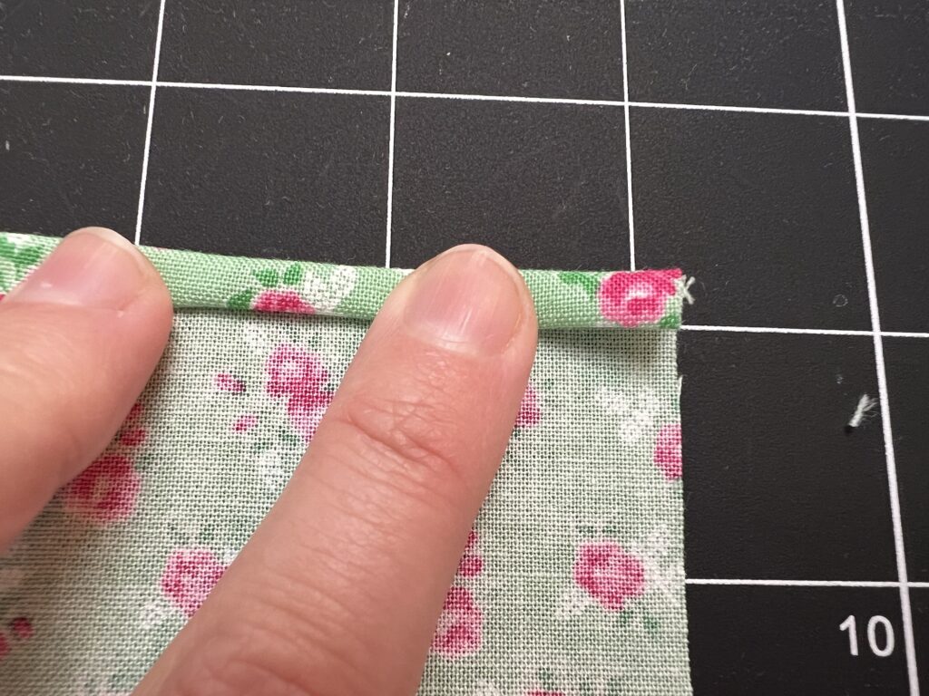 Hands folding floral fabric on a grid cutting mat, preparing it for a tiered skirt.