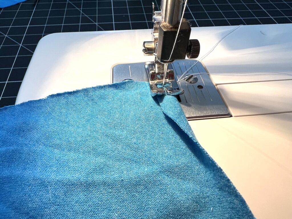 A sewing machine stitches blue fabric on a grid-patterned cutting mat.