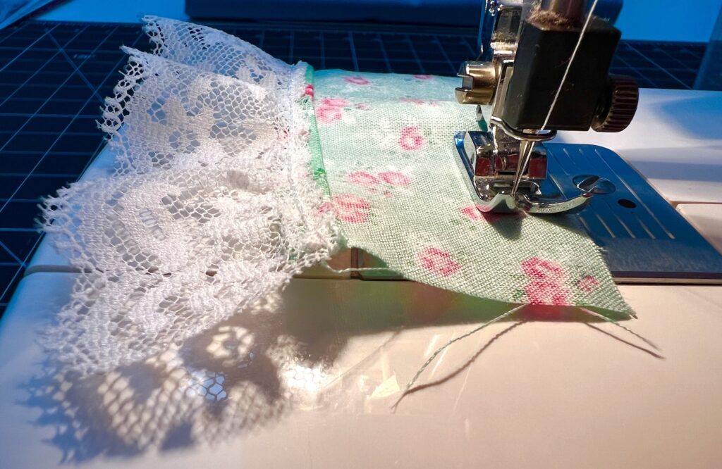 A sewing machine diligently stitches a piece of green floral-patterned fabric with lace trim, destined to become part of a charming tiered skirt, all set upon a grid-patterned cutting mat.