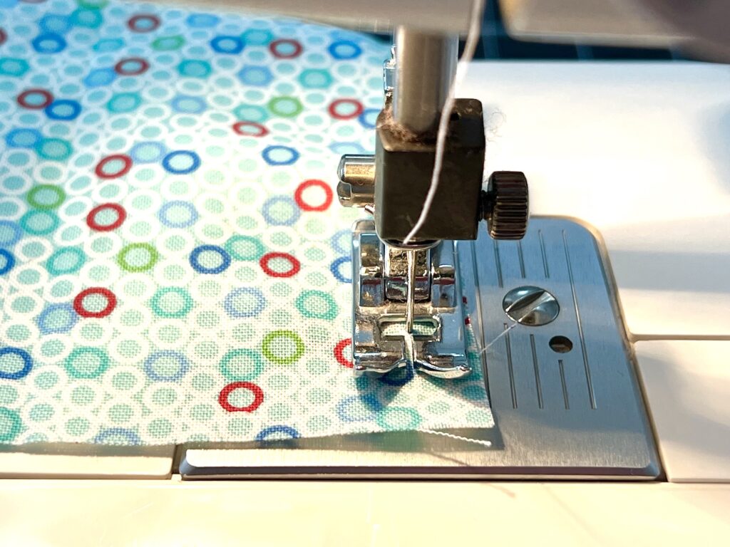 Close-up of a sewing machine needle stitching multicolored, patterned fabric.