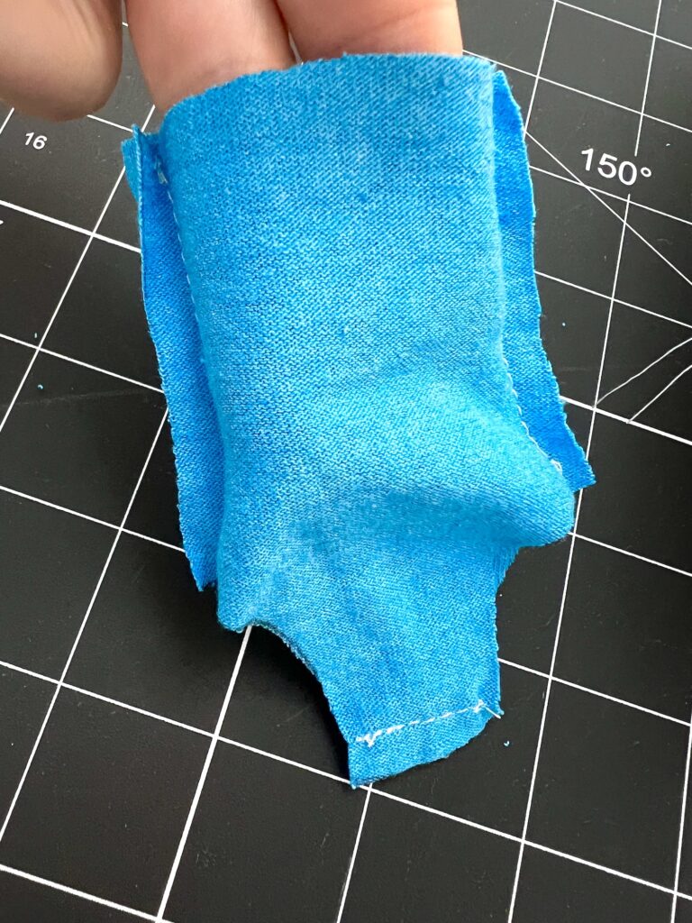 A hand holds a small piece of blue swimsuit fabric against a black grid cutting mat.