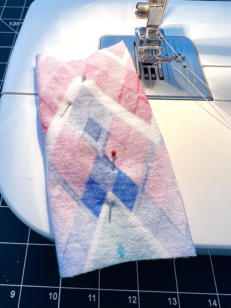 A piece of fabric with a geometric pattern is pinned and placed under a sewing machine needle.