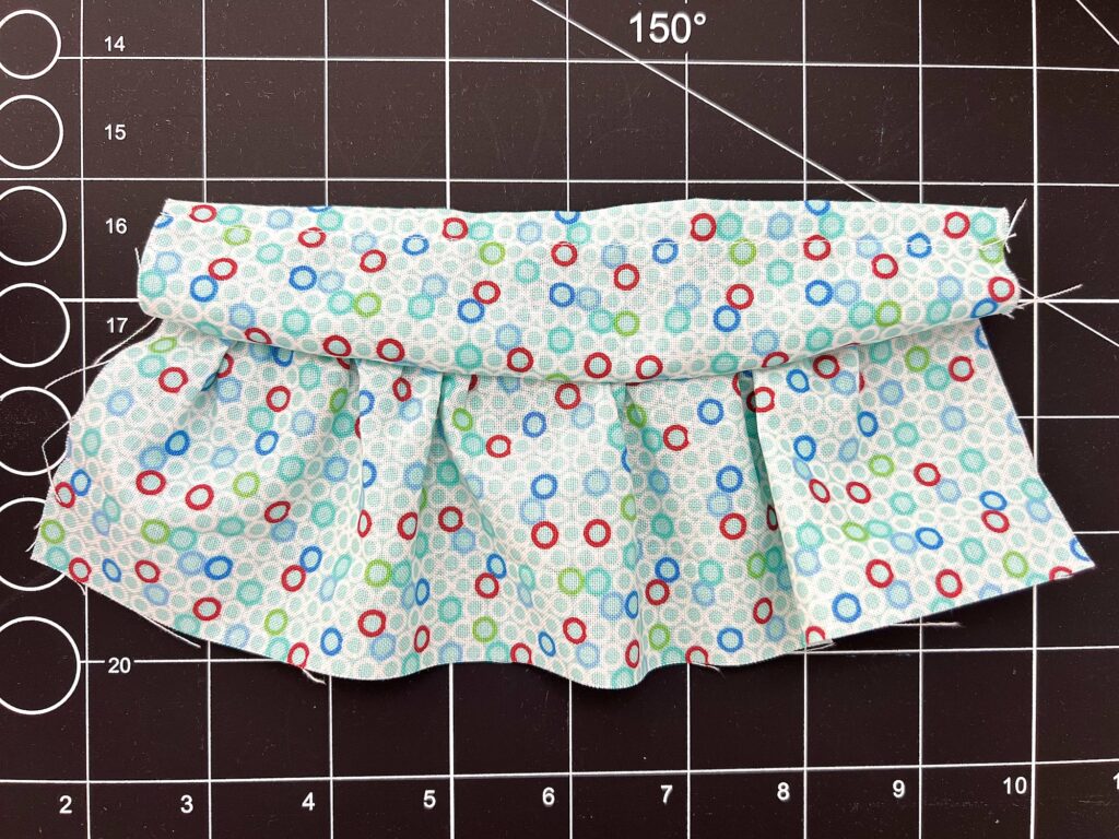 A piece of folded, pleated fabric with a pattern of multicolored circles on a measurement grid background.