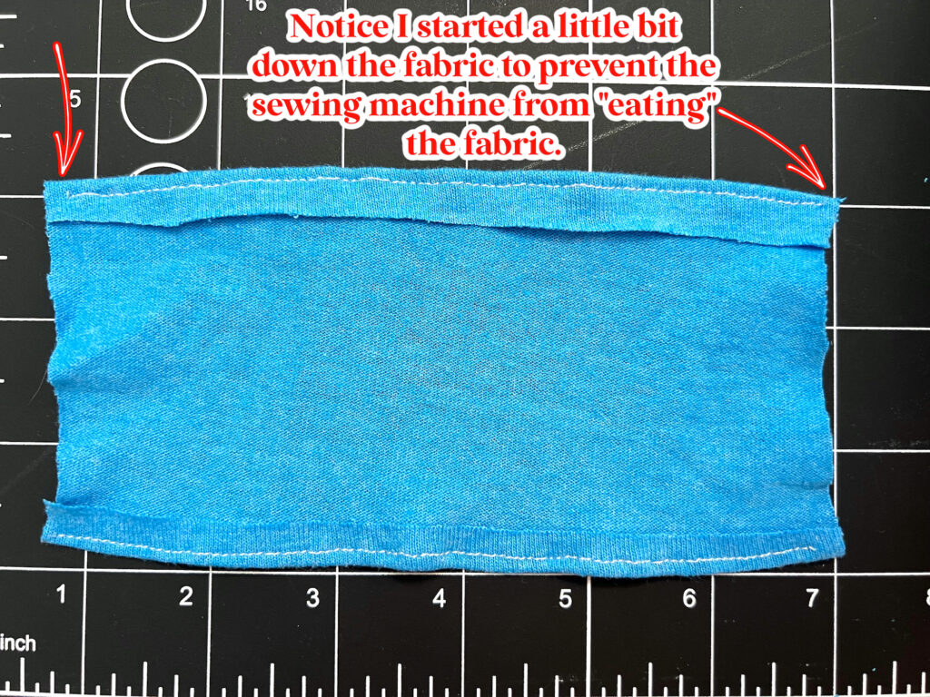 A piece of blue fabric with sewn edges is placed on a black cutting mat. Text indicates starting the seam before the edge to avoid the sewing machine catching the fabric.