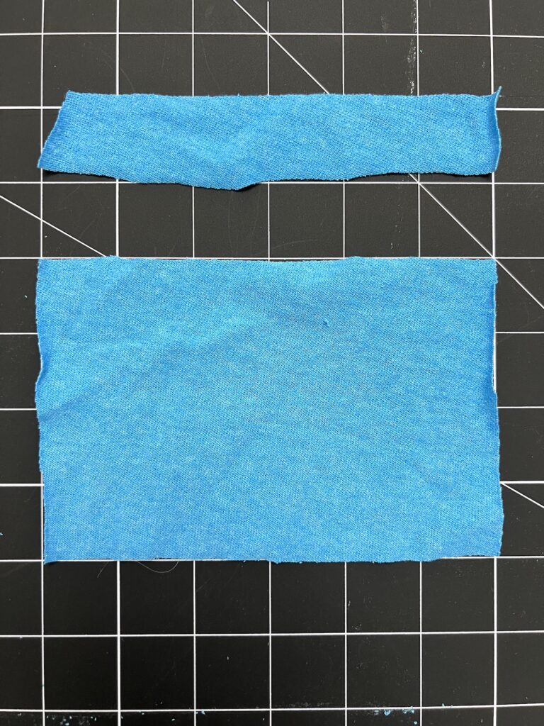 Two pieces of blue fabric on a black grid background; one rectangular and one long and thin.