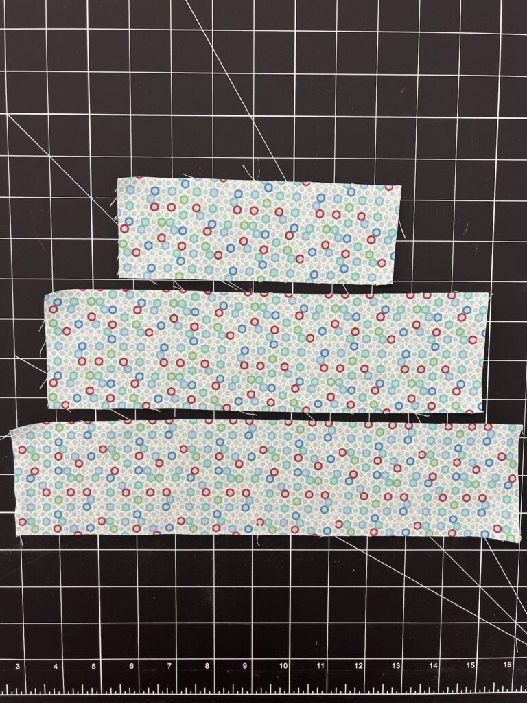 Three strips of fabric with a dot pattern on a black cutting mat with a grid layout.