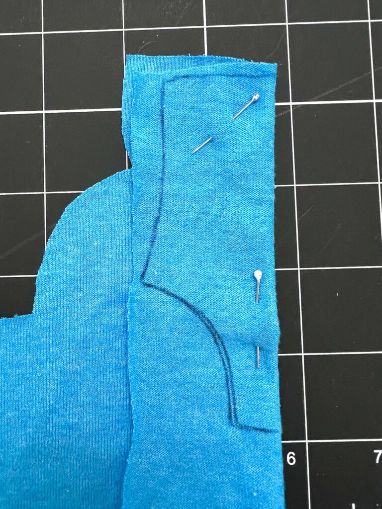 A blue fabric with a black outline and pins sits elegantly on a black grid cutting mat, ready to be transformed into a stylish swimsuit.