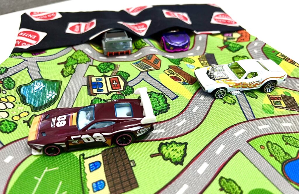 Toy cars zoom across a vibrant playmat featuring roads, trees, and buildings.