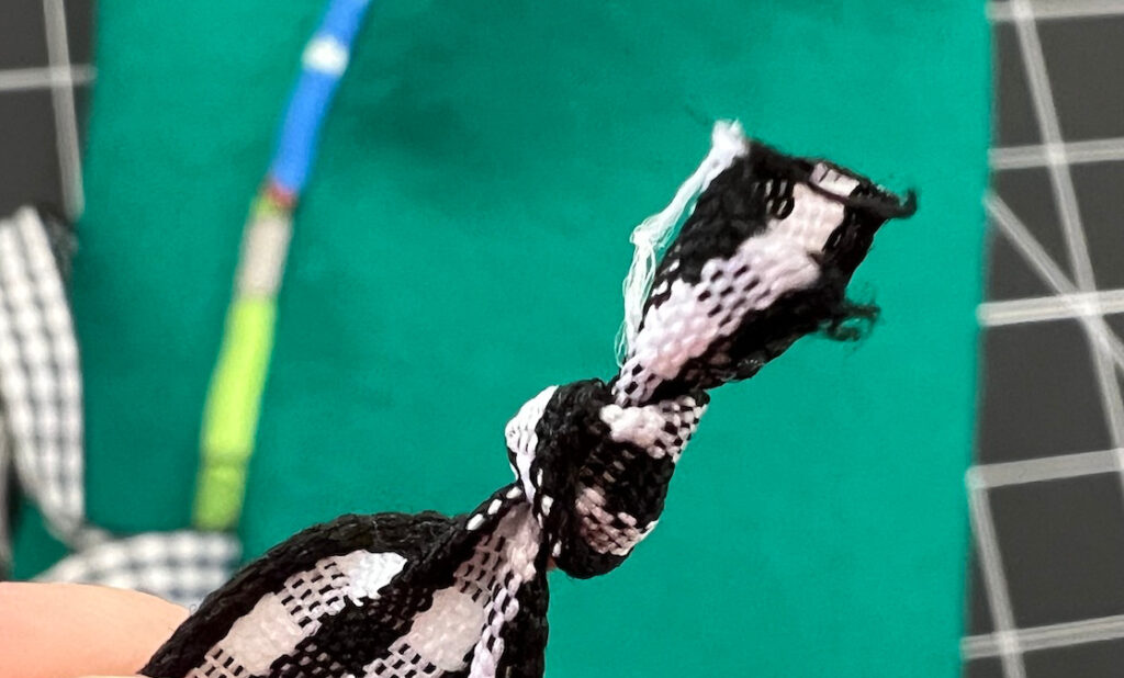 Close-up of a black and white checkered fabric tied in a knot, with a blurred green surface and hints of blue in the background.