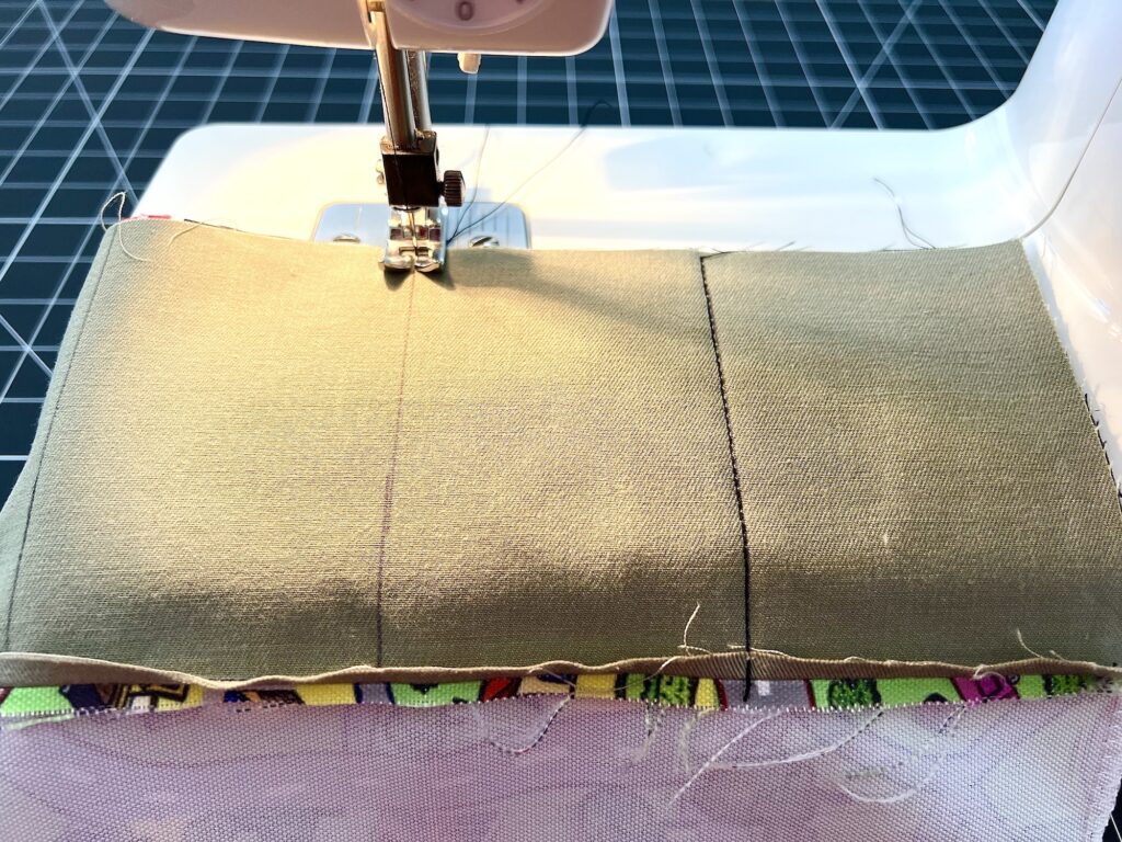 Sewing machine stitching two pieces of green fabric together, with colorful patterned fabric underneath.