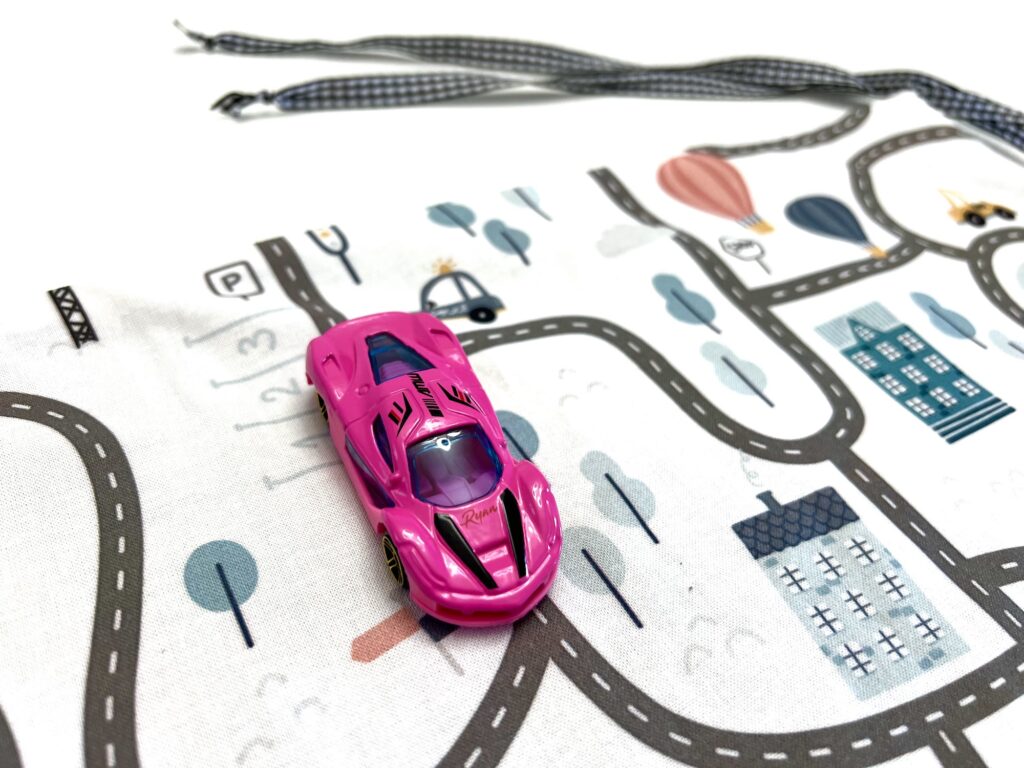 A pink toy car zooms around on a vibrant playmat, navigating roads lined with trees and colorful buildings.