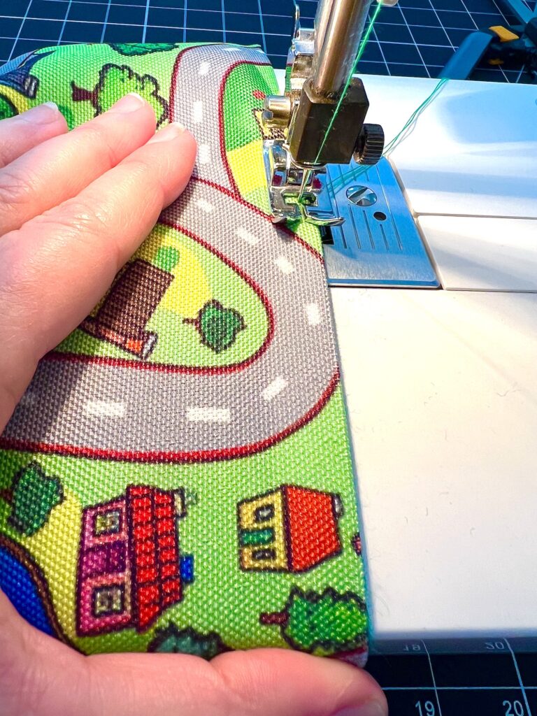 A person guides colorful fabric with a road and house pattern through a sewing machine.