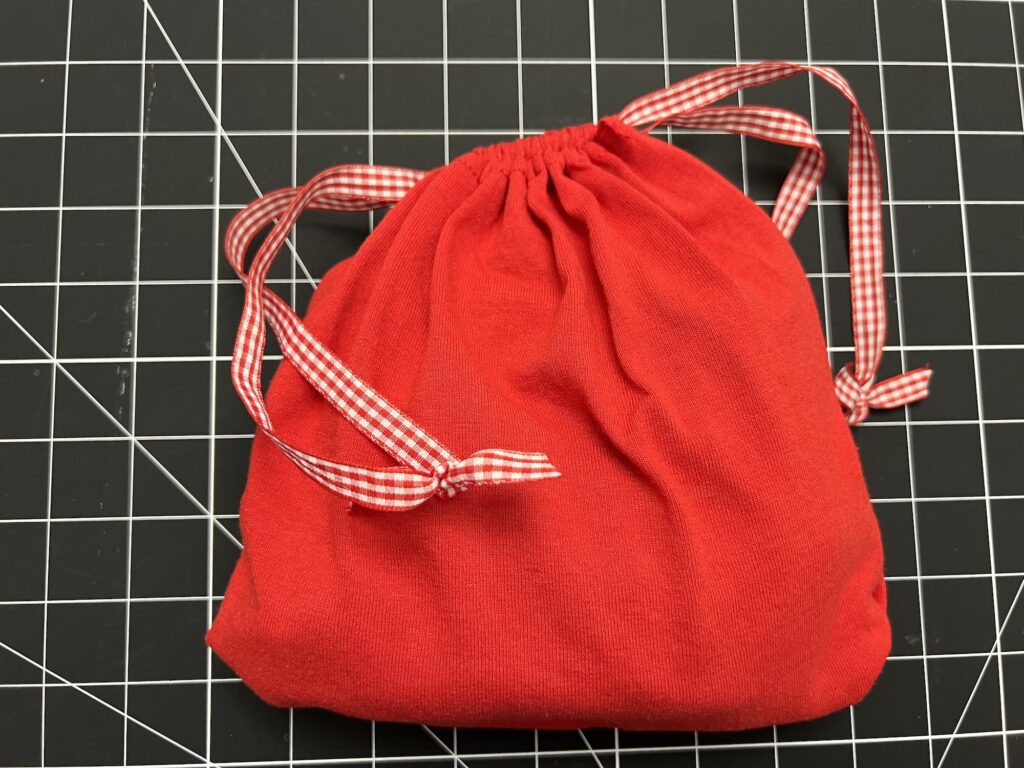 A red t-shirt bag with red and white gingham ribbon ties sits on a black grid cutting mat.