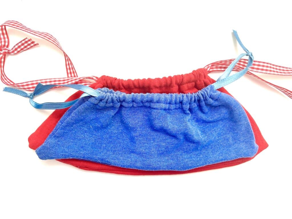 Two fabric face masks lie flat on a white background, one blue with blue ribbons and one red with red and white checked ribbons—perfectly coordinated like t-shirt sleeve drawstring bags for your everyday essentials.
