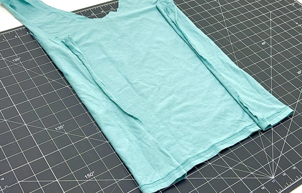 A light blue t-shirt, ideal for crafting a t-shirt bag, is folded in half on a black cutting mat with measurement markings.