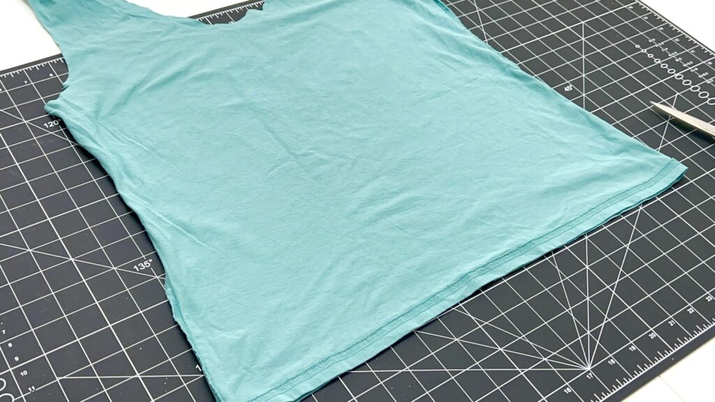 A light blue t-shirt bag, styled like a tank top, is laid flat on a black grid cutting mat with scissors partially visible on the right.