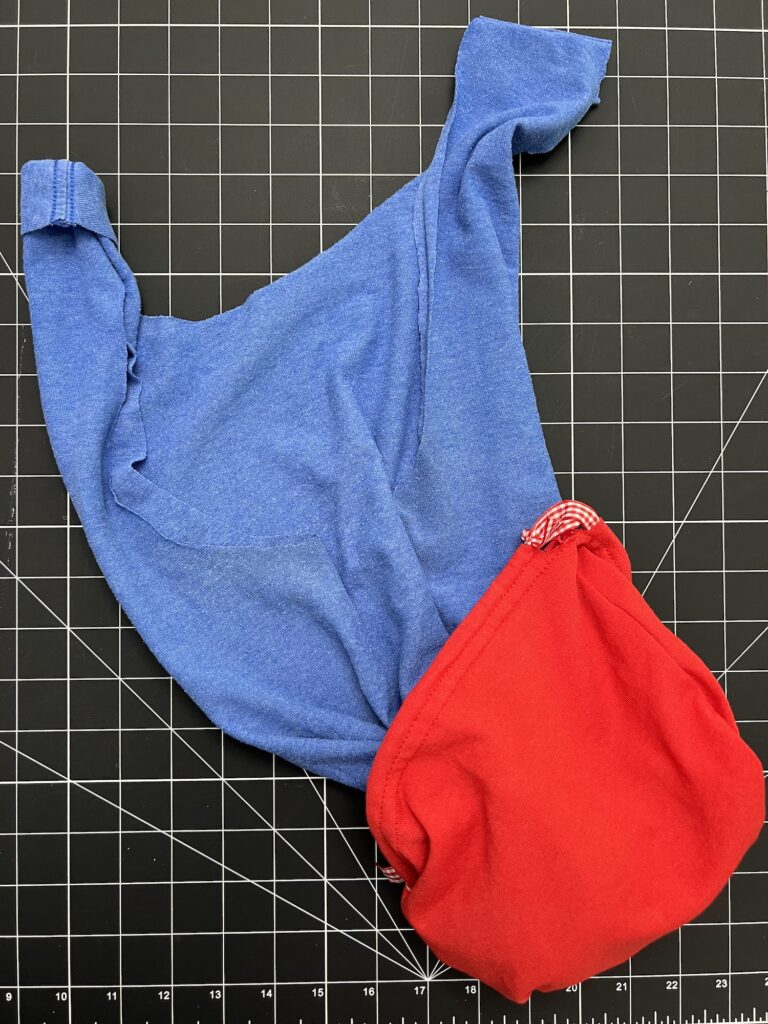 A blue t-shirt and a red fabric item are laid out on a black grid cutting mat, ready to be transformed into a t-shirt bag.