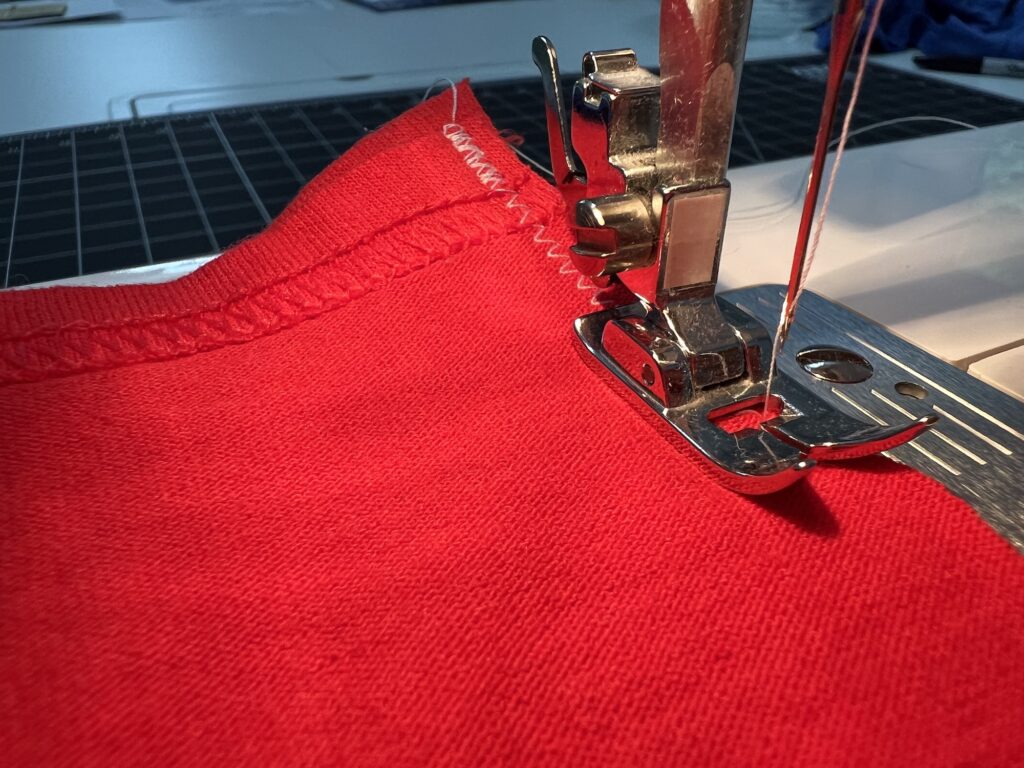 Close-up view of a sewing machine stitching a zigzag pattern on bright red fabric, perfect for crafting a unique t-shirt bag.