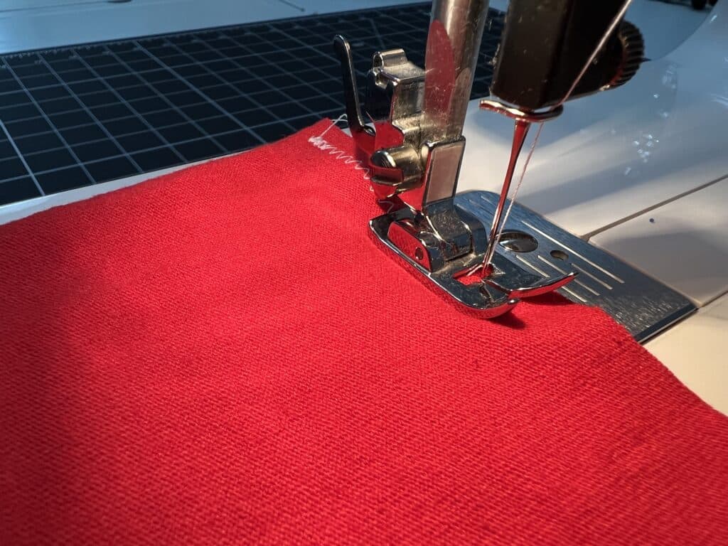Close-up of a sewing machine stitching a piece of red fabric, with the needle and presser foot clearly visible, ideal for creating t-shirt sleeve drawstring bags.