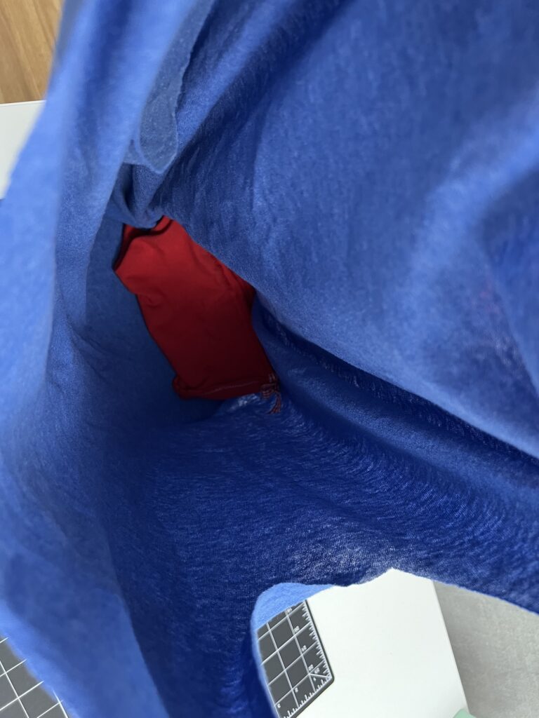 View inside a blue t-shirt bag with a red item at the bottom, placed on a surface with a visible cutting mat nearby.