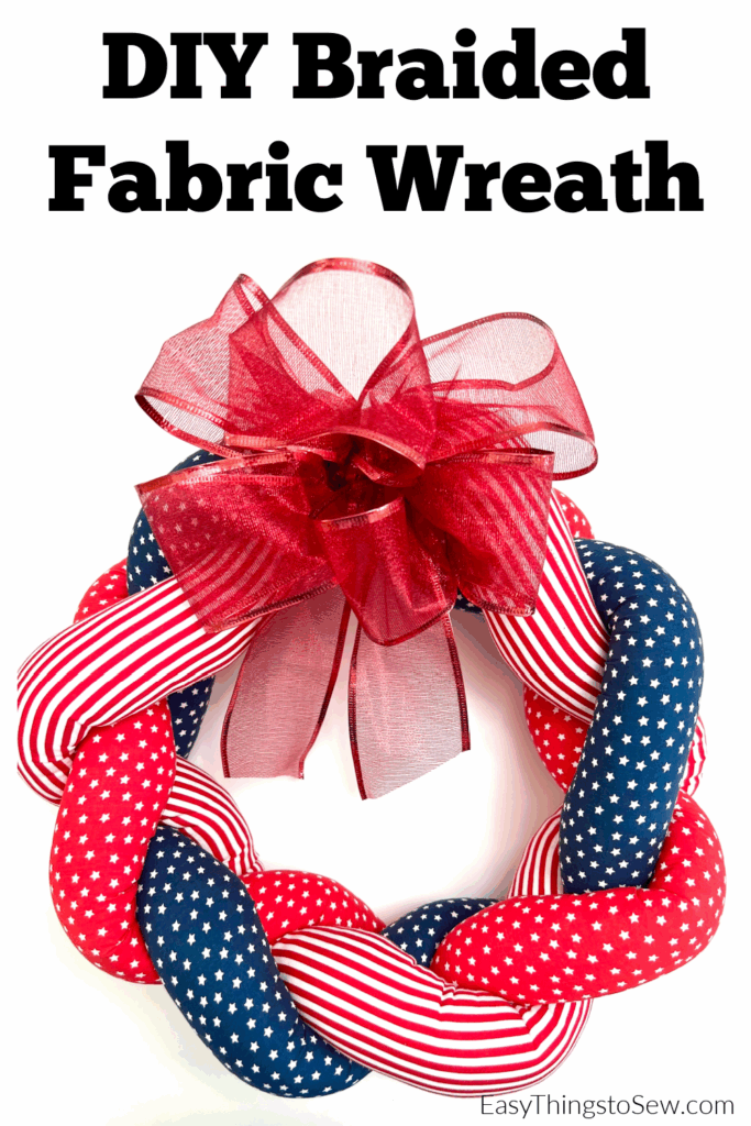 A braided fabric wreath with red, white, and blue star and stripe patterns, topped with a large sheer red bow. Text above reads, "DIY Braided Fabric Wreath.