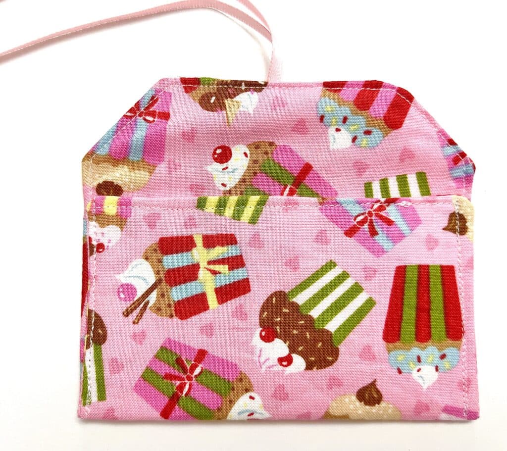 A small pink fabric pouch with a cupcake pattern, featuring an open flap and a white ribbon attached.