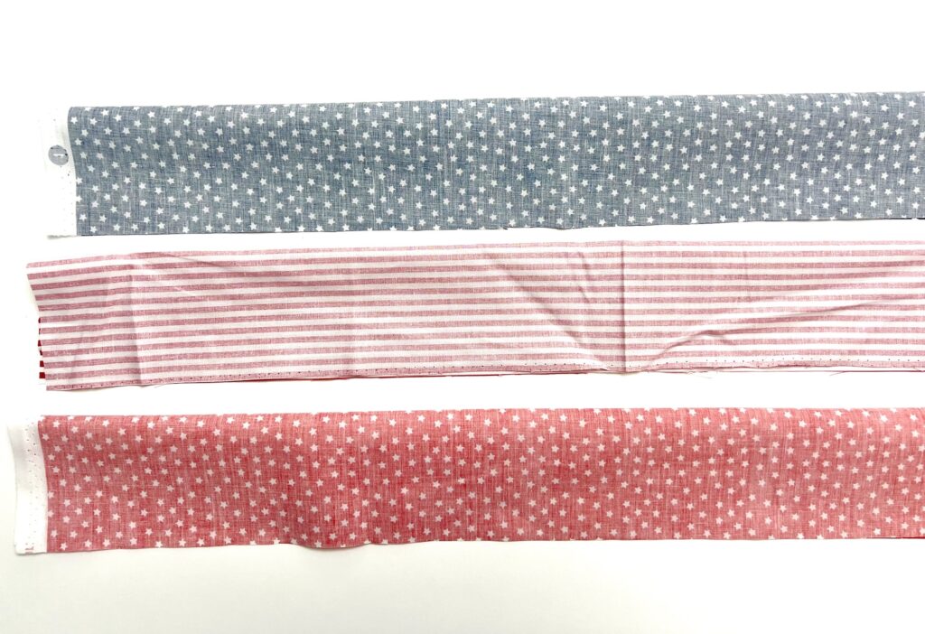 Three strips of fabric on a white surface: blue with white stars, pink with white stripes, and red with white stars.
