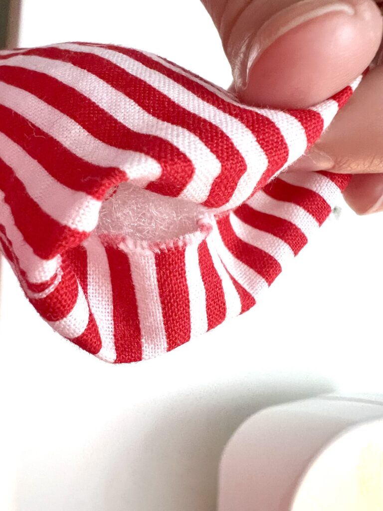 A hand holds a red and white striped fabric item with a visible hole showing exposed stuffing inside.